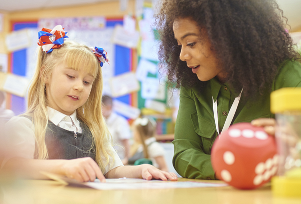 A primary aged schoolgirl sits with her teacher in a one to one math session