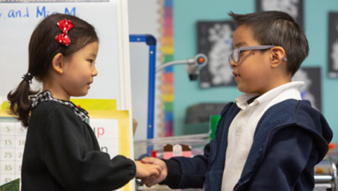 Image of two young elementary students shaking hands in a classroom