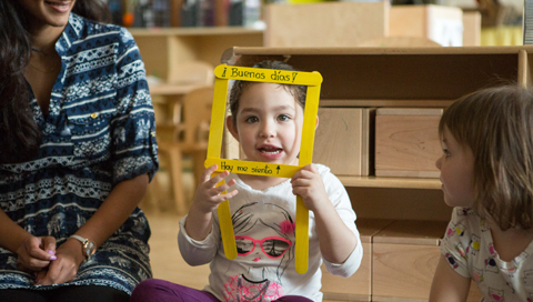 Image of a young girl with her face framed by a toy stating Buenos Dias