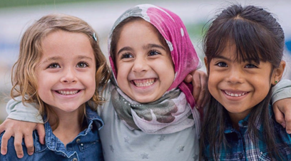 Three young girls of different ethnicities smiling with arms around one another