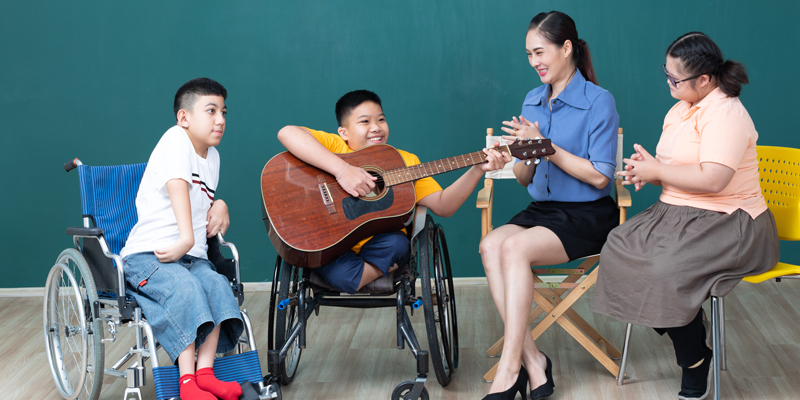 Asian disabled children in wheelchairs and woman teacher enjoying and playing guitar