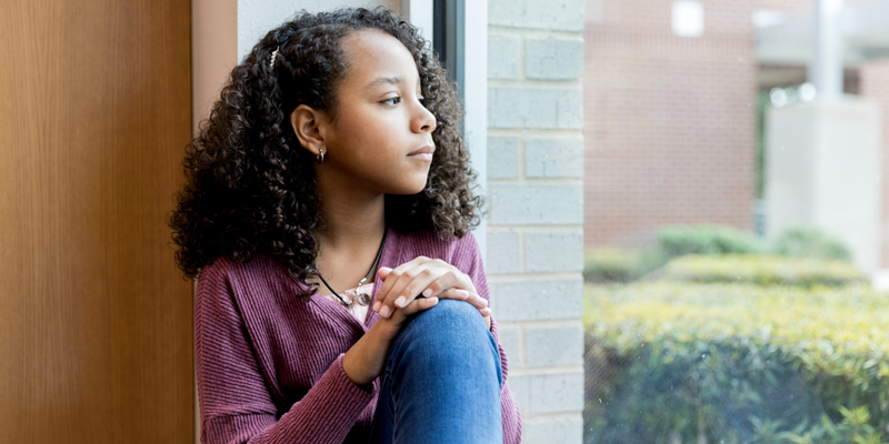 Lonely preteen schoolgirl looking through the window while at school