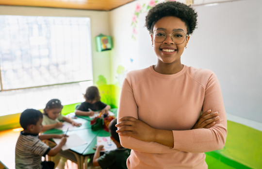 Image of happy African American preschool teacher smiling in a classroom at the school