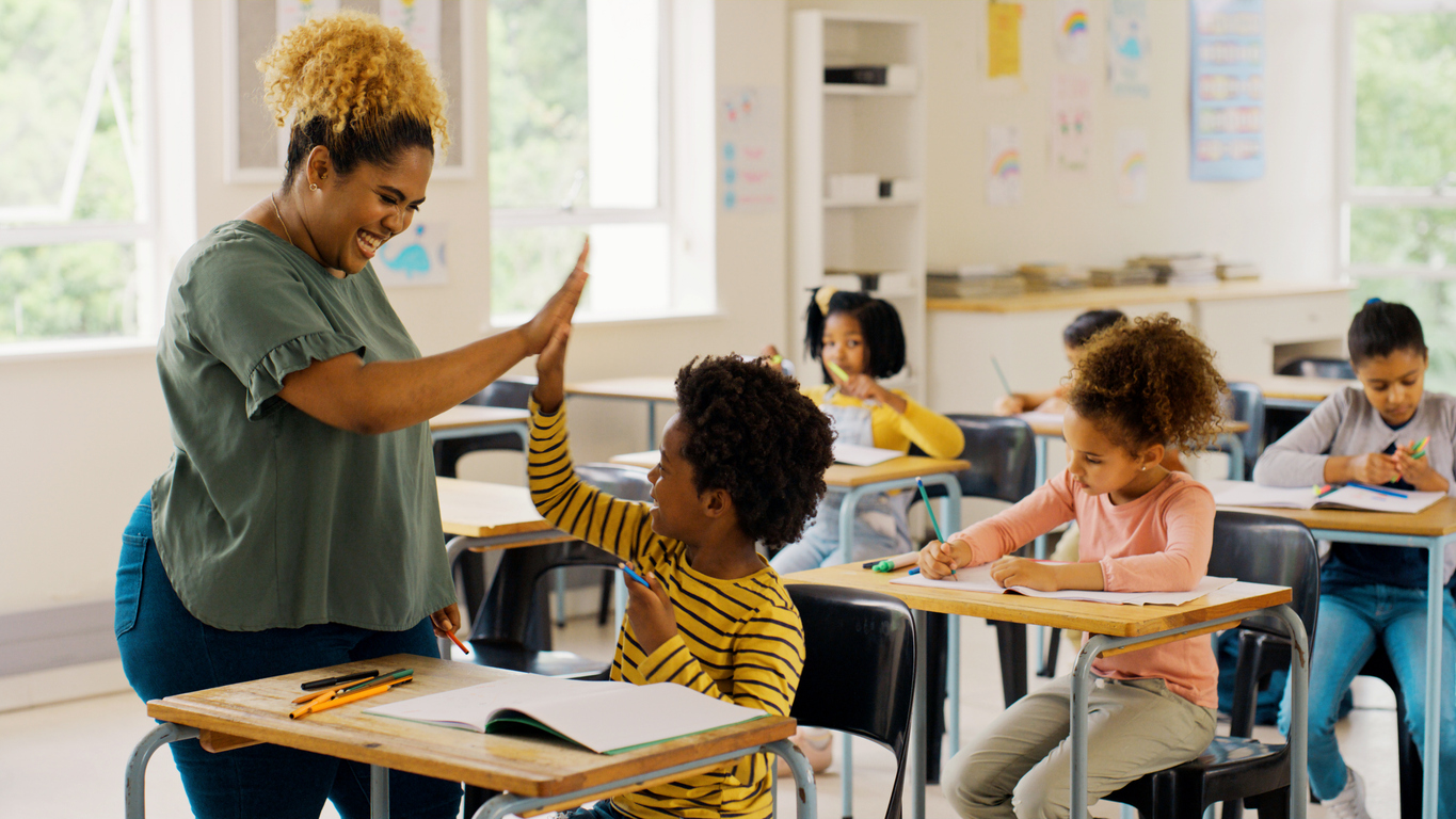 Happy female teacher giving high fives to young students in a classroom